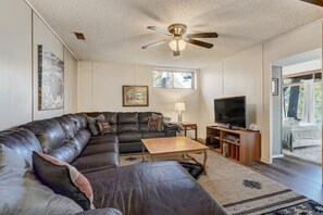 A living room with a sectional sofa, a television, a ceiling fan, and a large window.