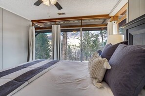 Une chambre avec un grand lit, un ventilateur de plafond et une vue sur les arbres par la fenêtre.