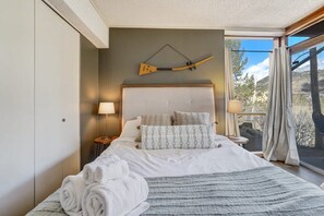 Une chambre à coucher avec un grand lit, une tête de lit, deux lampes de chevet, une fenêtre avec des rideaux et un objet décoratif fixé au mur.