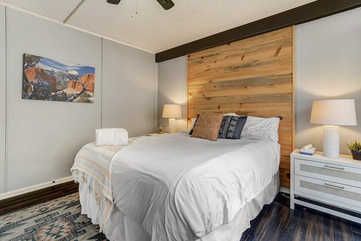 A bedroom with a bed, nightstands, a wooden headboard, a painting, and a patterned rug.