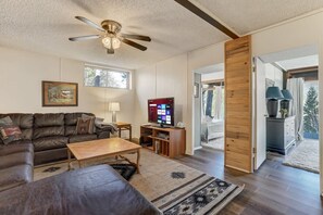 A living room with a leather sofa, a wooden coffee table, a TV, and a ceiling fan.