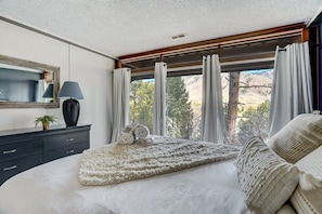 A bedroom with a bed, a bedside table, a lamp, and a window with curtains.