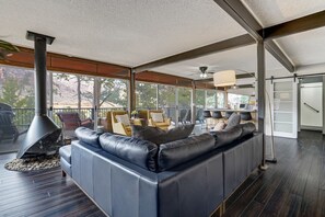 Un salon moderne doté d’un grand canapé en cuir noir, d’une cheminée et offrant une vue sur l’extérieur grâce à de grandes fenêtres.