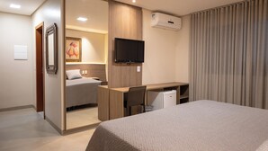 A hotel room with a bed, a desk, a chair, a television, and an air conditioning unit.