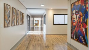 A hallway with wooden flooring, framed artworks on the walls, and a large colorful painting on the right.