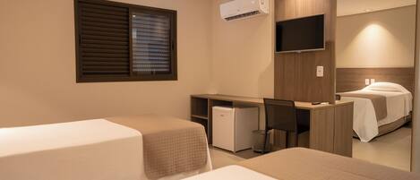 A hotel room with two beds, a desk, a chair, a TV, and an air conditioning unit.