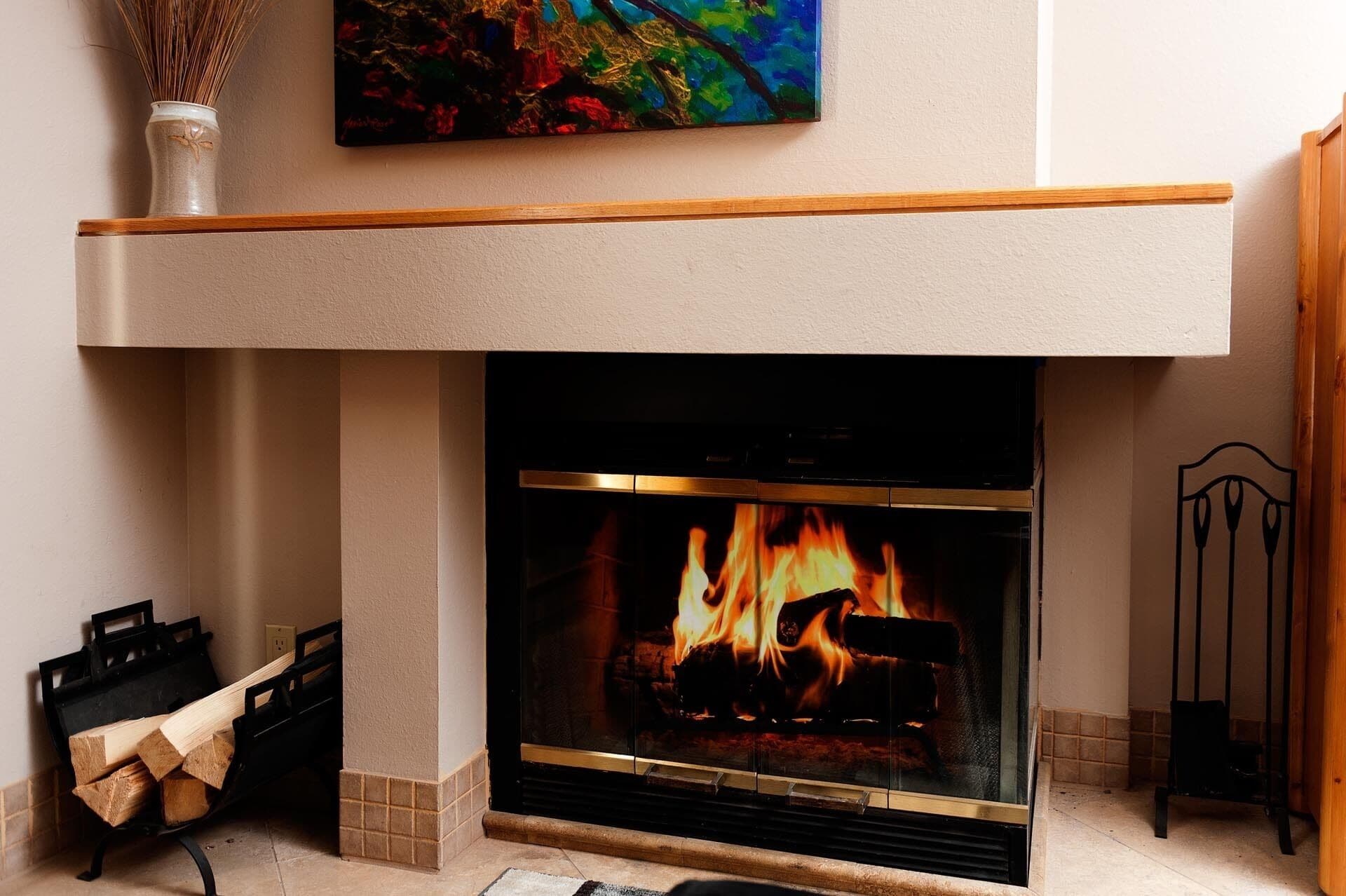 Een moderne haard met een glazen voorpaneel, een houten bovenplaat en een vaas met gedroogde planten erop.
