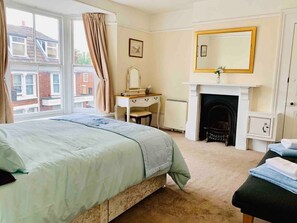 A bedroom with a bed, a dresser, a mirror, a fireplace, and a window with curtains.