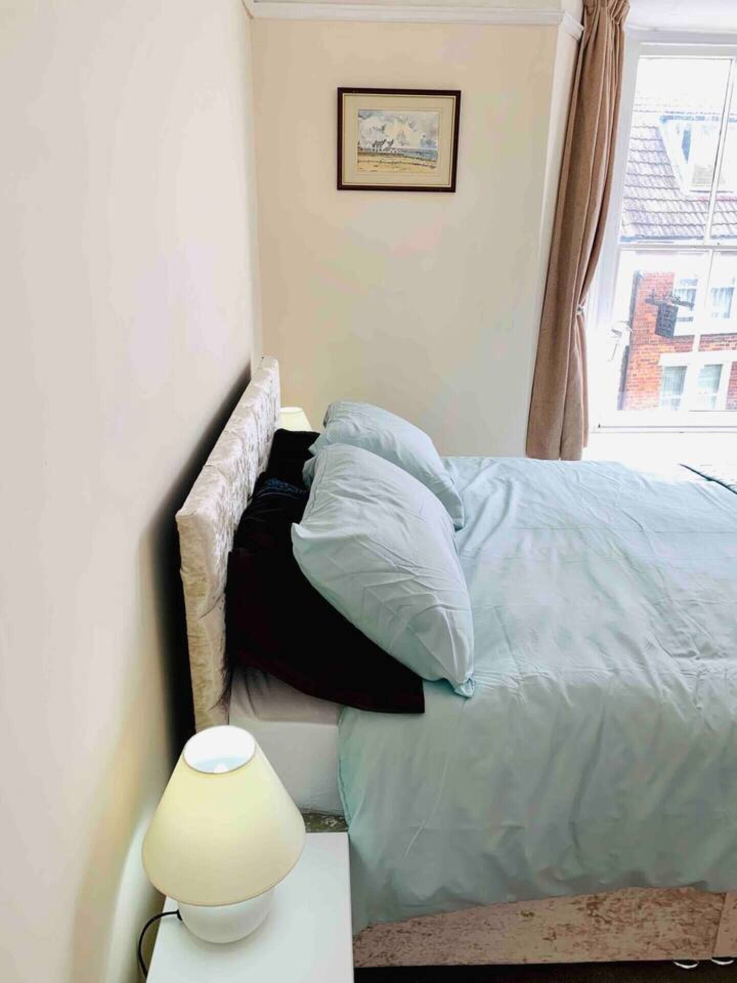 Un dormitorio con cama, una lámpara de noche y un cuadro en la pared.