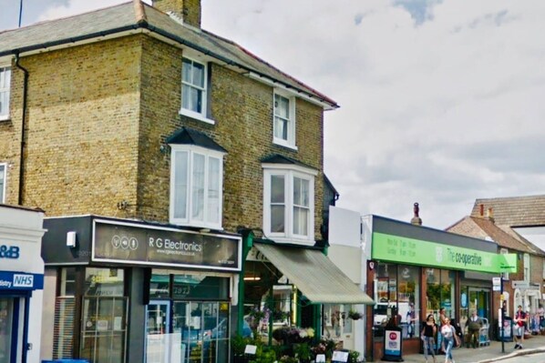 A street view with a brick building, a shop with a green sign, and a visible sign for R G Electronics.