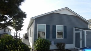 A single-story house with a gabled roof, a front porch, and a small front yard with a car parked in the driveway. - Direct Bay front home with 2 community pools and tennis (Ocean City)