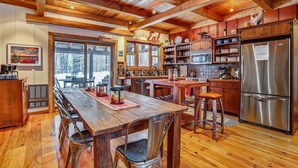 A spacious kitchen with wooden cabinets, a stainless steel refrigerator, and a dining area with a wooden table and metal chairs. - This completely renovated Canaan Valley chalet offers it all, and more! (Canaan Valley)