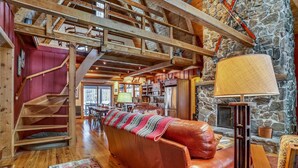 A cozy cabin interior with a wooden staircase, a leather sofa, a stone fireplace, and a dining area. - This completely renovated Canaan Valley chalet offers it all, and more! (Canaan Valley)