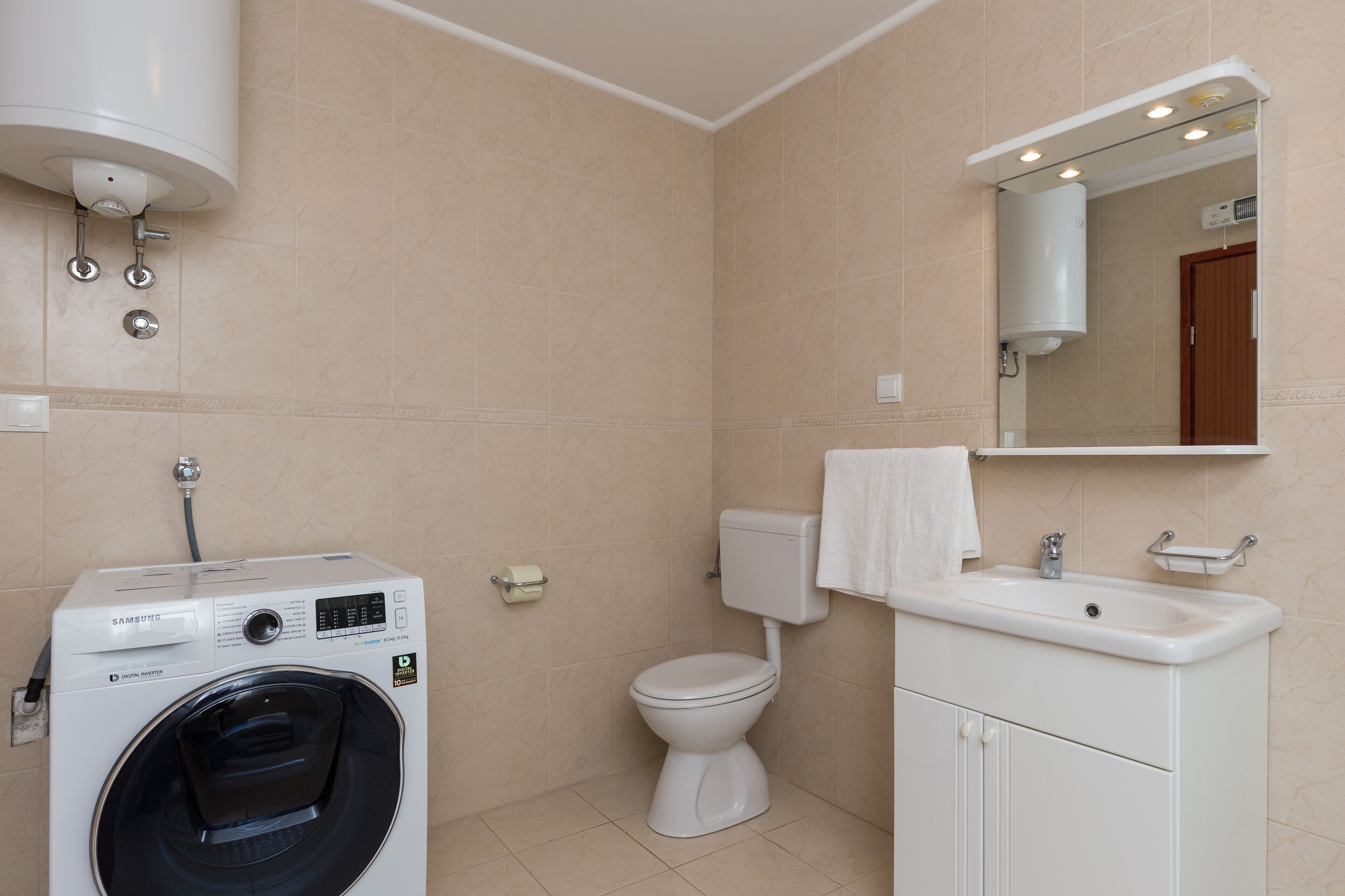 A bathroom with a washing machine, toilet, sink, and mirror.