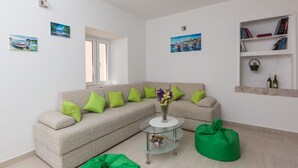 Een moderne woonkamer met een beige modulaire bank, groene kussens, een glazen salontafel en een groene kruikzak.