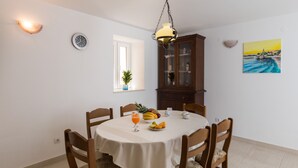 Een eetgedeelte met een ronde tafel, stoelen, een klok, een kast en een schilderij aan de muur.