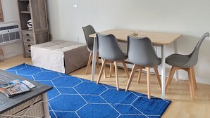 A modern living room with a flat-screen TV mounted on the wall, a wooden dining table with four chairs, a blue hexagonal rug, and a sofa. - Sandy Jack's on 80th, 1 bedroom.  Steps to the beach and pool! Stocked! (Ocean City)