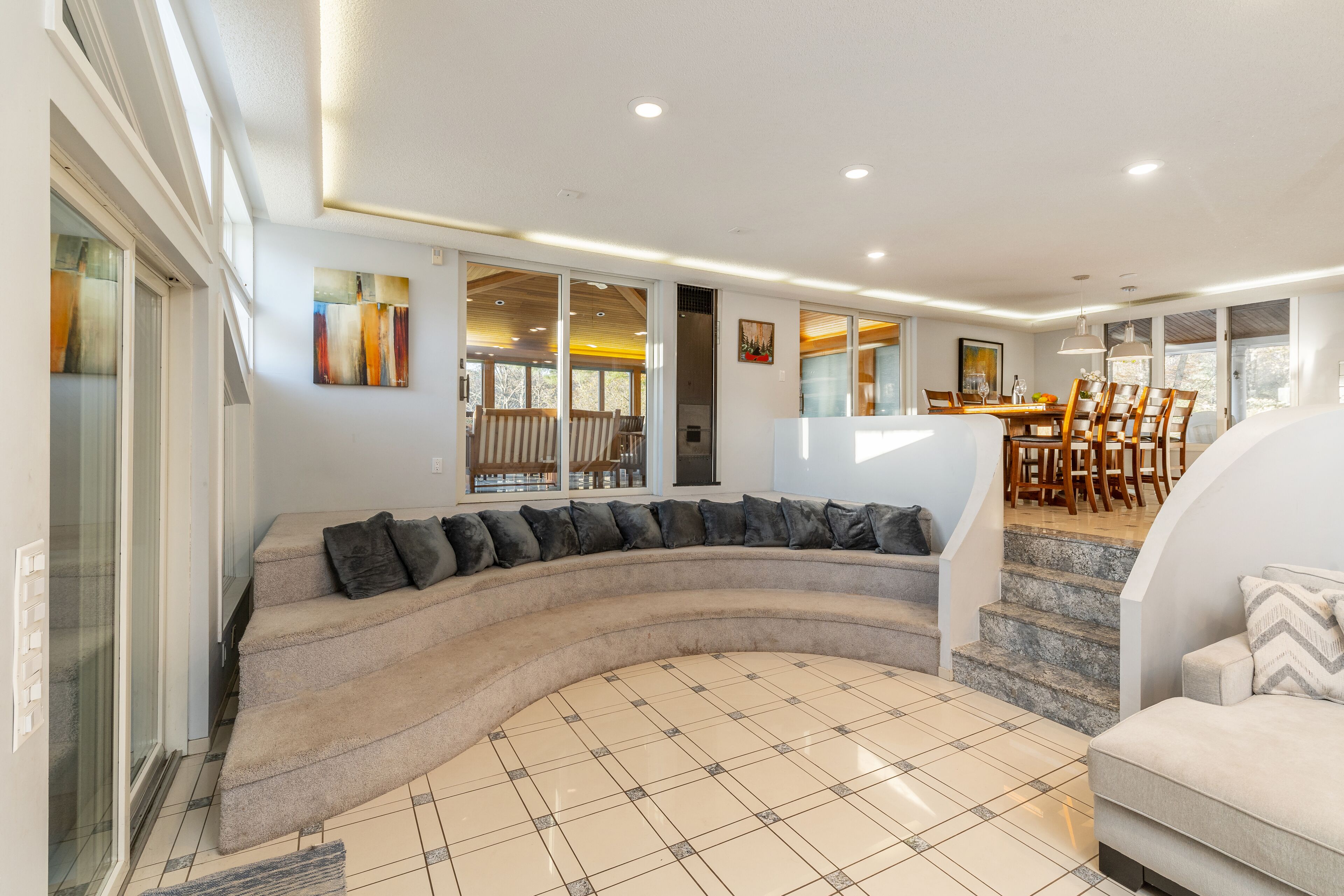 A modern living room with a curved sectional sofa, a dining area with wooden chairs, and a staircase leading to another level.