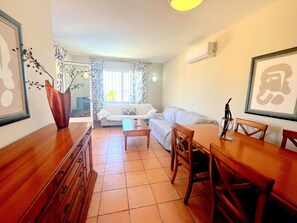 Een woonkamer met een bank, een eettafel met stoelen, een salontafel, een houten kast en een raam met gordijnen.