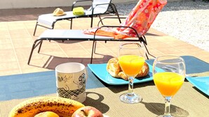 A table set with breakfast items including fruits and juice, with a view of a fenced area and a chair in the background.