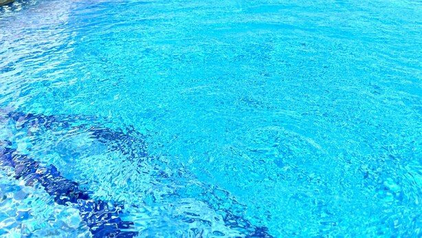 A swimming pool with clear blue water, surrounded by lounge chairs and a balustrade.