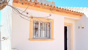 A white building with a tiled roof, a window with metal bars, and a door.