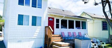 A two-story house with a red door and a small porch with plastic chairs.