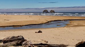 A beach with a large rock formation in the distance, sandy shore, and a small stream. - Beachfront! Walk the short path to the Beach, or enjoy the waves from the Deck (Rockaway Beach)