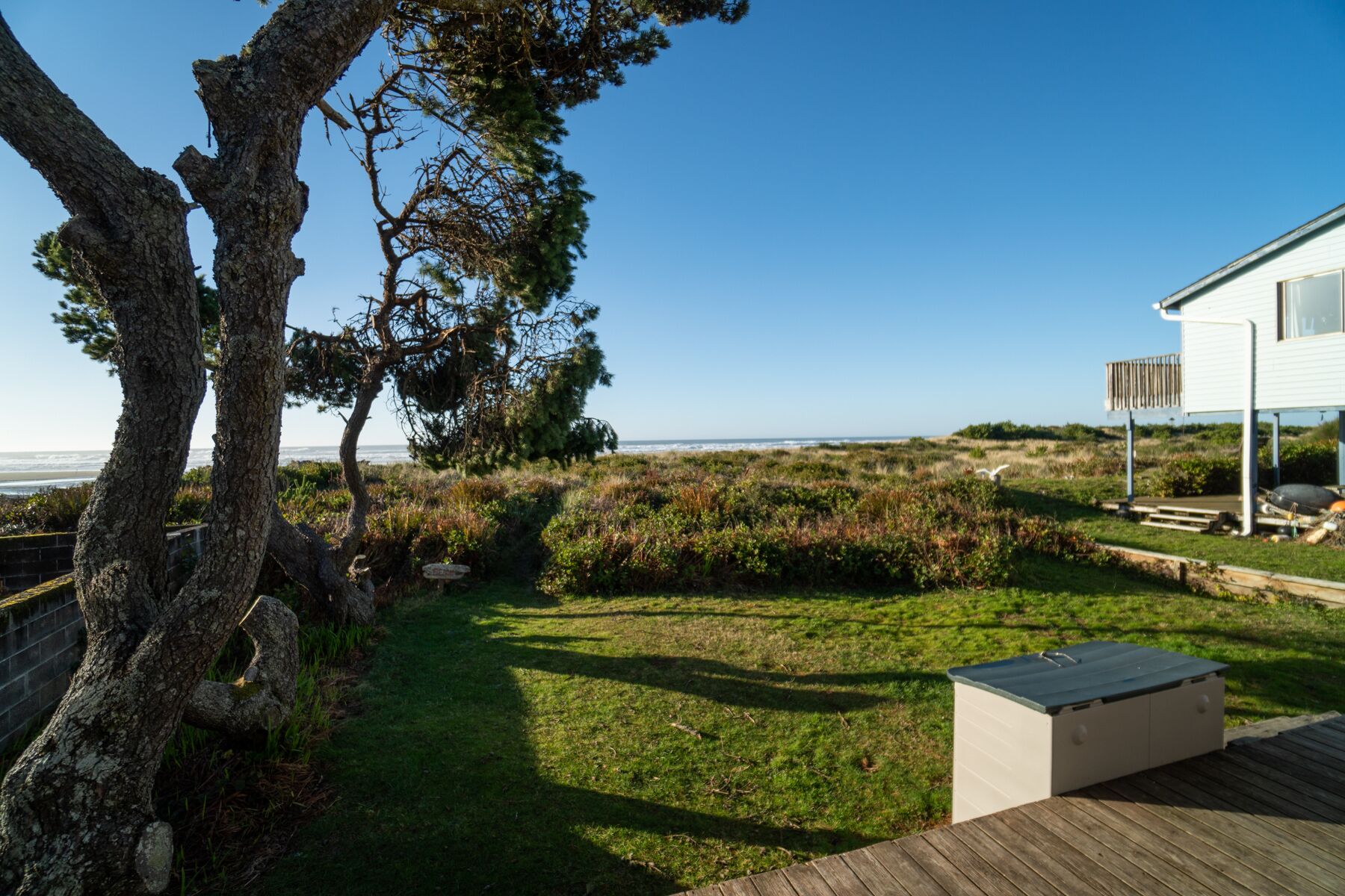 A coastal property with a grassy lawn, a wooden deck, and a white house with a balcony.