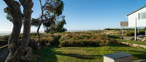 A coastal property with a grassy lawn, a wooden deck, and a white house with a balcony.