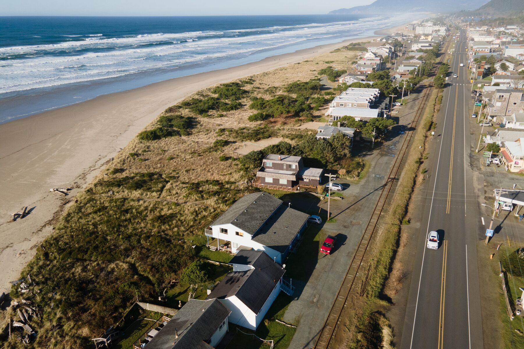 An aerial view of a coastal road with houses on one side and a beach on the other.