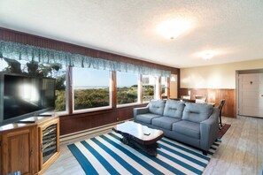 A living room with a large TV, a grey sofa, a wooden coffee table, and a striped rug.