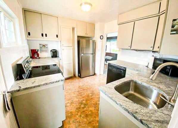 Una cocina con armarios blancos, un refrigerador de acero inoxidable, lavavajillas y encimeras de granito.