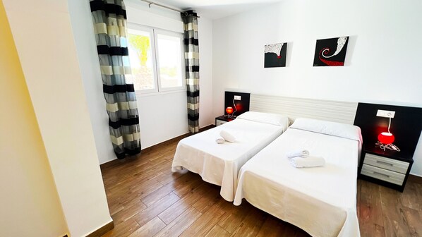 Camera d'albergo con due letti, una finestra con tende, un comodino con lampada e un quadro appeso al muro.