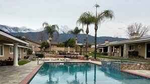 Uma piscina com borda de pedra, palmeiras e vista para montanhas ao fundo.