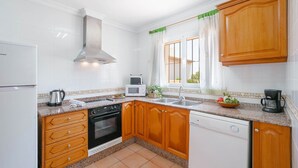 Une cuisine avec des meubles de rangement en bois, une cuisinière, un lave-vaisselle et une fenêtre avec des rideaux.