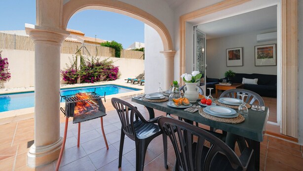 Un espace repas avec vue sur la piscine, un barbecue et une table dressée pour le repas.