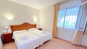 A hotel room with two beds, a wooden headboard, bedside lamps, a window with curtains, and a view of greenery outside. - 0361 Villa Monte Javea Laurel (Javea / Xàbia)