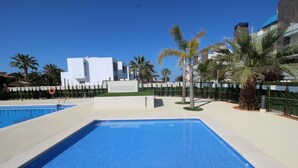 Une piscine à l’eau d’un bleu cristallin, entourée de palmiers et de bâtiments modernes.