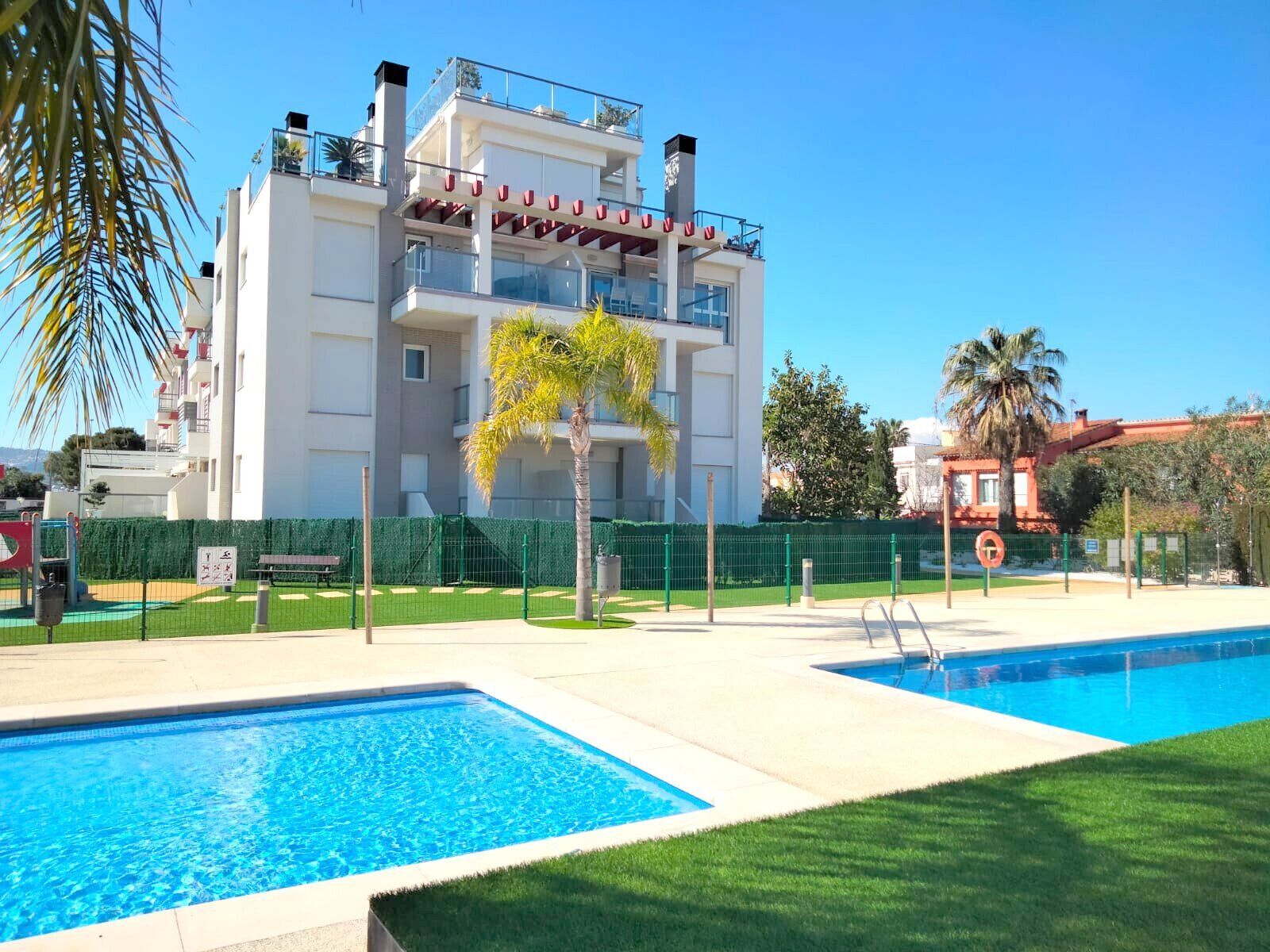 A modern building with a pool area, including two swimming pools and a green lawn.