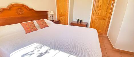 A neatly made bed with a wooden headboard, a bedside table with a lamp, and two wooden doors in the background.