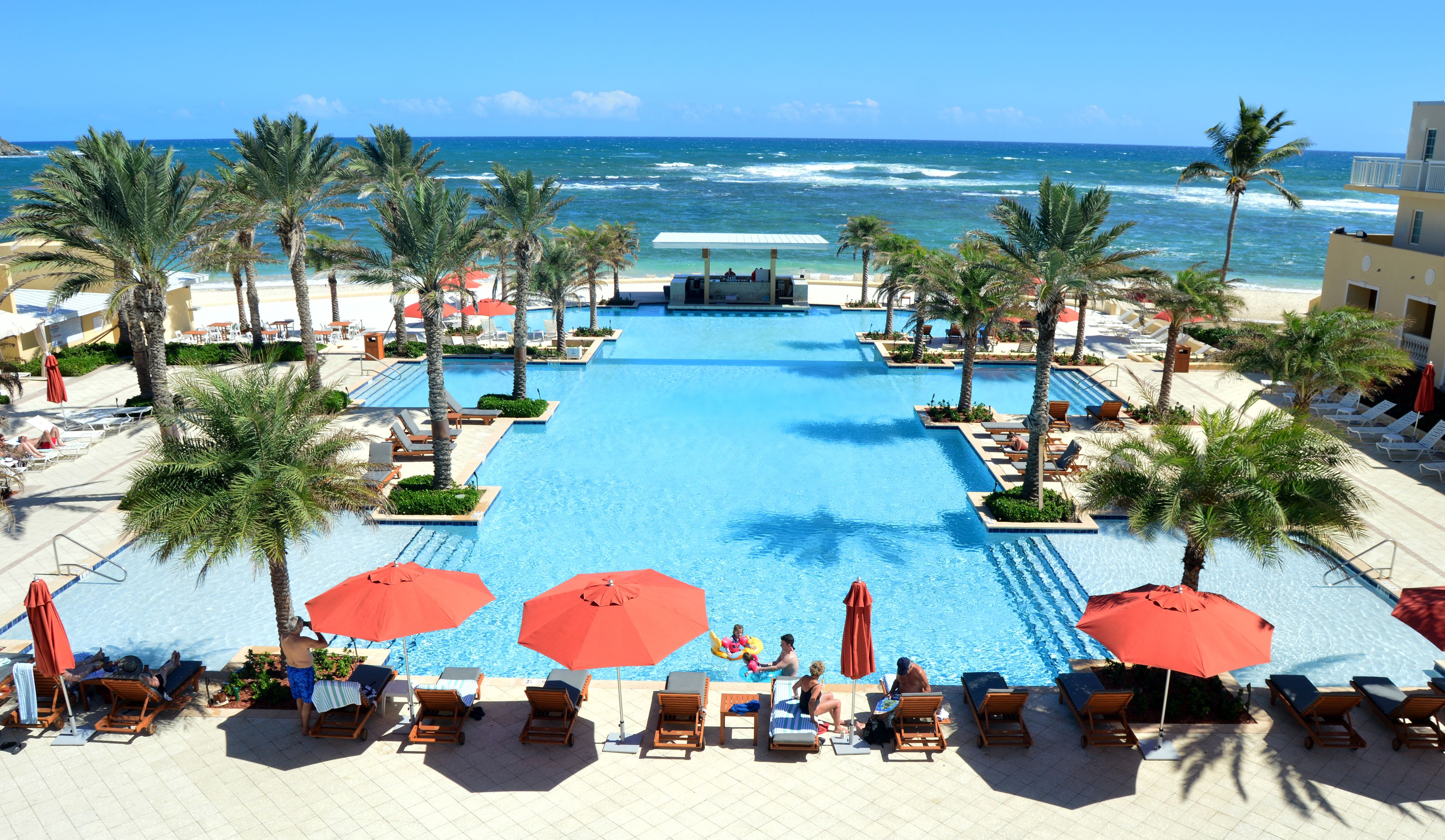 A pool area with lounge chairs and umbrellas, overlooking the ocean.
