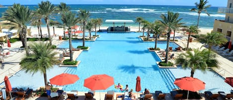 A pool area with lounge chairs and umbrellas, overlooking the ocean.