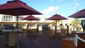 Eine Holzterrasse mit Sitzgelegenheiten im Freien, roten Sonnenschirmen und einem Poolbereich.