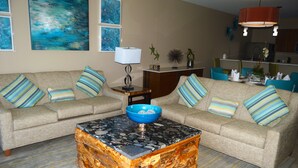 A living room with a beige sofa, striped pillows, a coffee table with a blue bowl, and abstract art on the wall. - Building A- Condo - Direct Ocean Front Views...directly on the beach. (Sint Maarten)