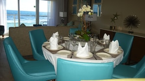 A dining area with a view of the ocean, a table set with white napkins and plates, and teal chairs. - Building A- Condo - Direct Ocean Front Views...directly on the beach. (Sint Maarten)