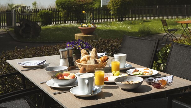 Una mesa de desayuno al aire libre con diversos platos, entre ellos frutas, pan y bebidas.