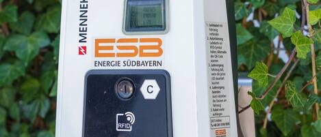 Ein MENNEKES Energiemessgerät mit digitaler Anzeige, RFID-Lesegerät und einem QR-Code, vor einem Hintergrund aus grünen Efeu-Blättern.