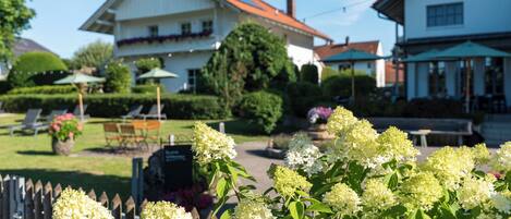 A garden with hydrangea flowers in the foreground, a white building with a red roof in the background, and a green umbrella.