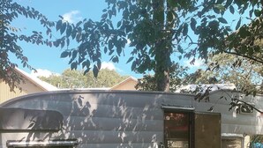 Une caravane ancienne dotée d’une porte, d’une petite fenêtre et d’un panneau métallique sur le côté.